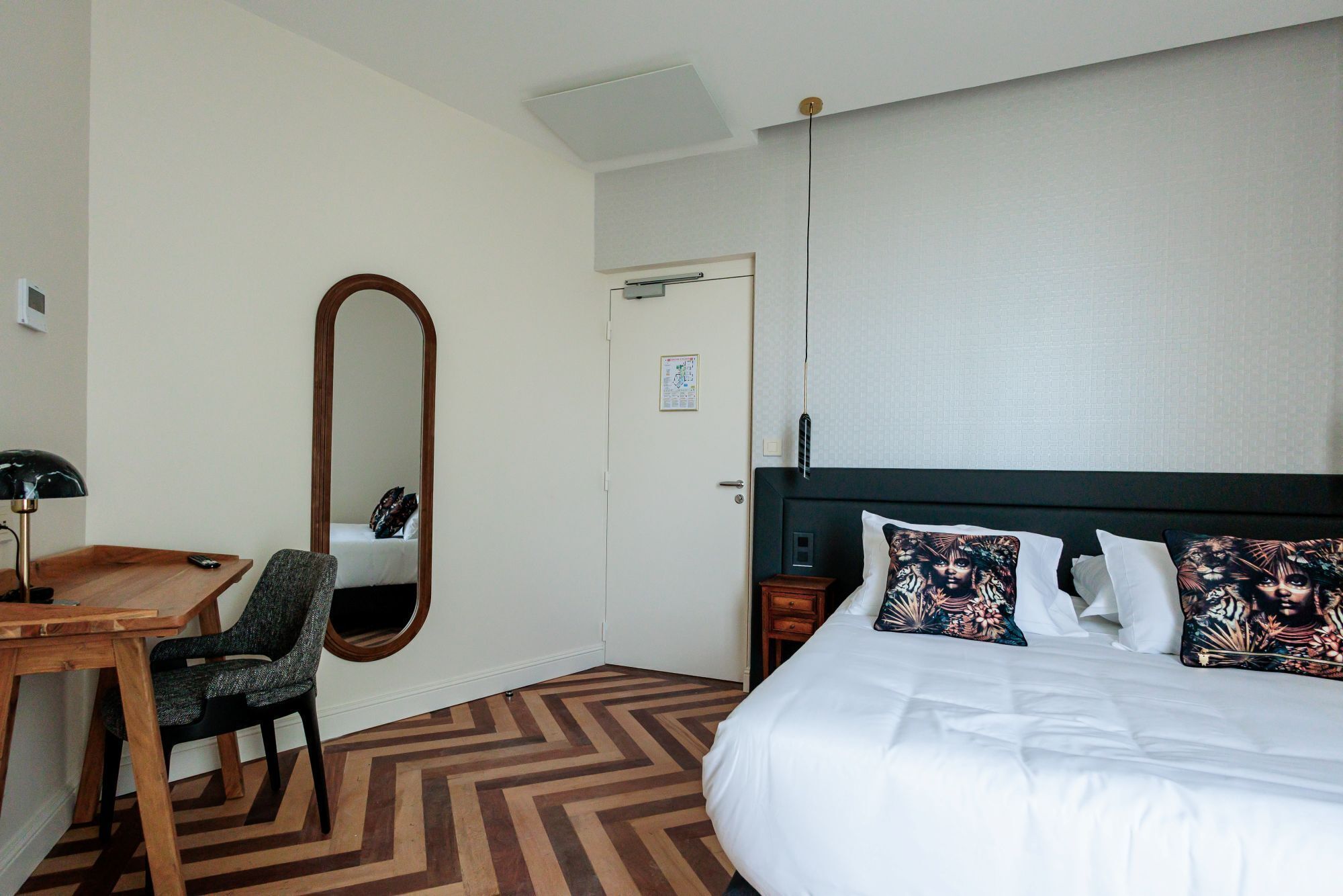 Una habitación de hotel con una cama, una silla, un escritorio, un espejo y una puerta.