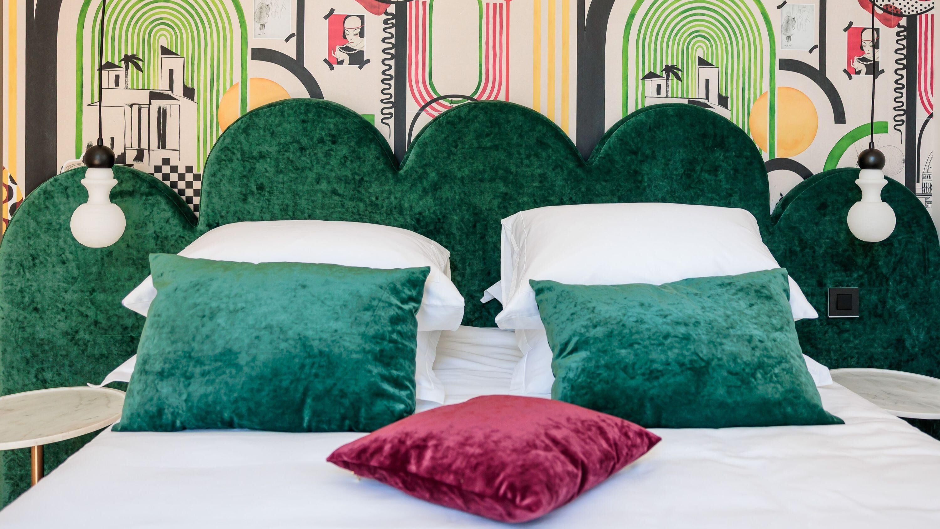 Un lit avec une literie verte et blanche, deux oreillers verts et un oreiller rouge.