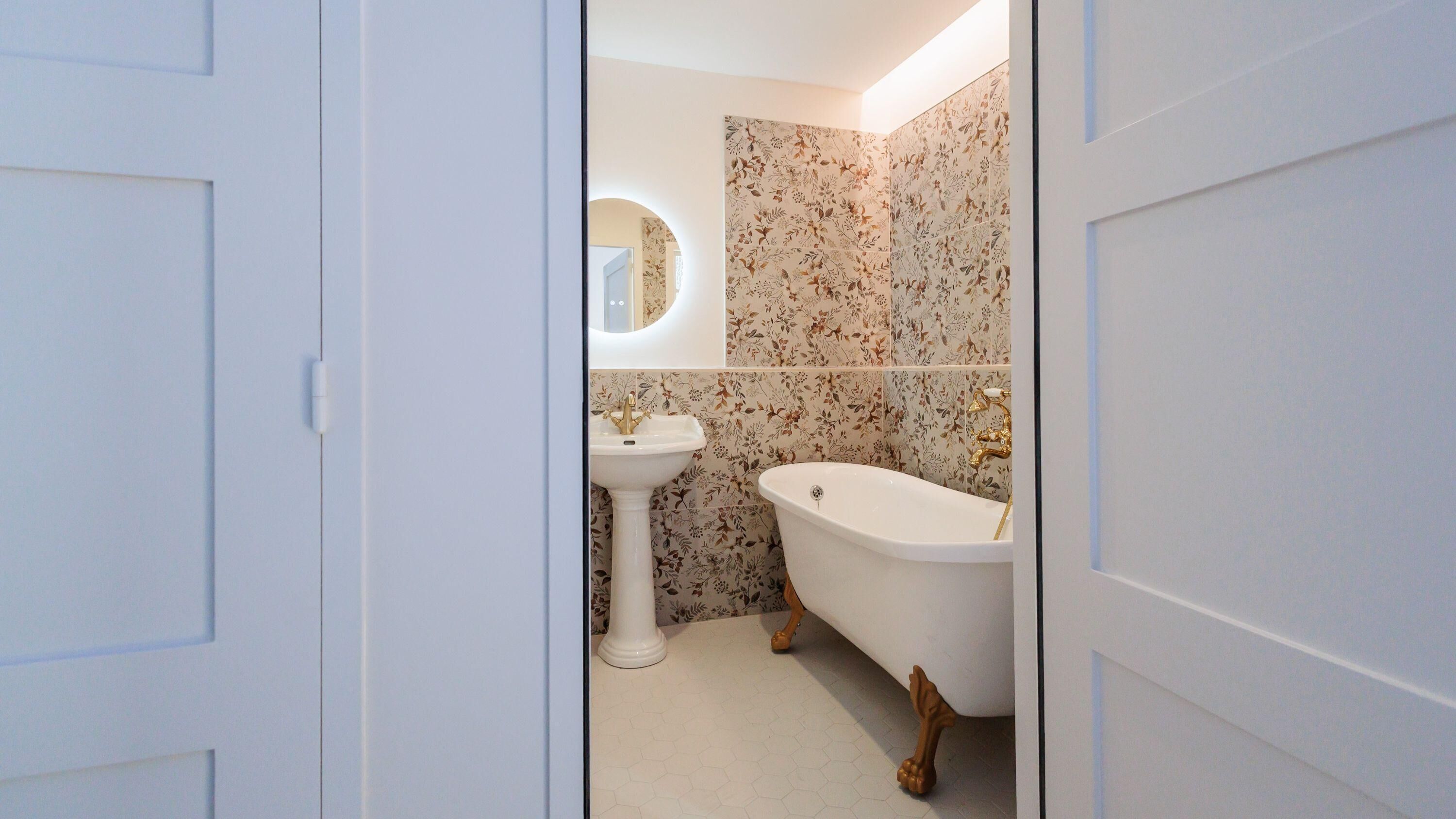 A bathroom with a white sink, a freestanding bathtub, and floral patterned tiles.