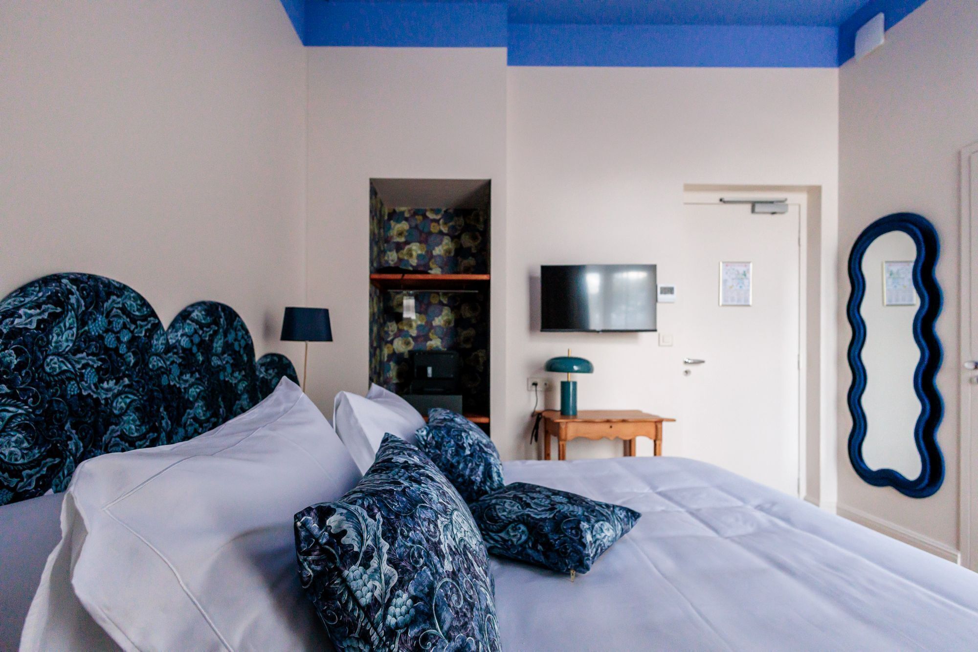 A bedroom with a bed, pillows, a TV, a mirror, and a door.