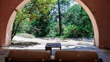 An outdoor seating area with two chairs and a table, framed by an archway overlooking a forested area.