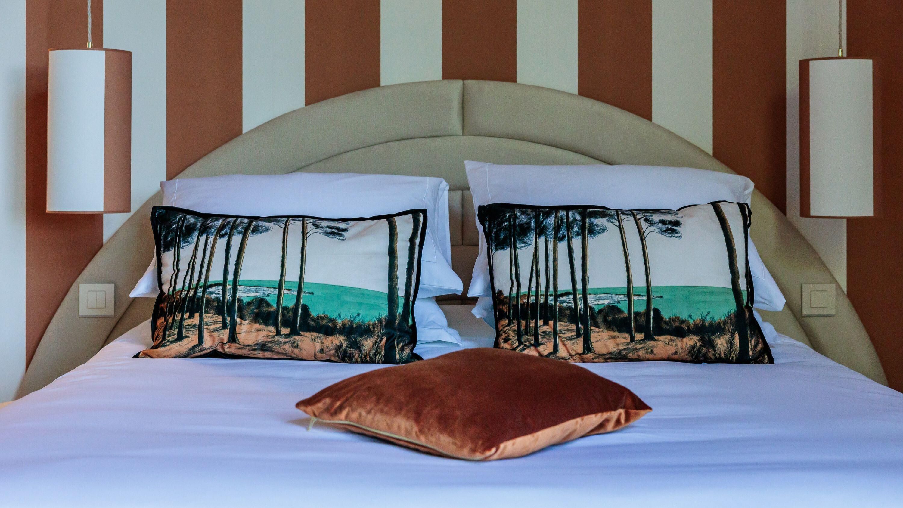 A bed with two pillows featuring a beach scene, a beige headboard, and two hanging lamps.