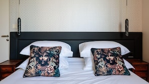 A bed with white linens, two black nightstands, and two decorative pillows with a jungle theme.
