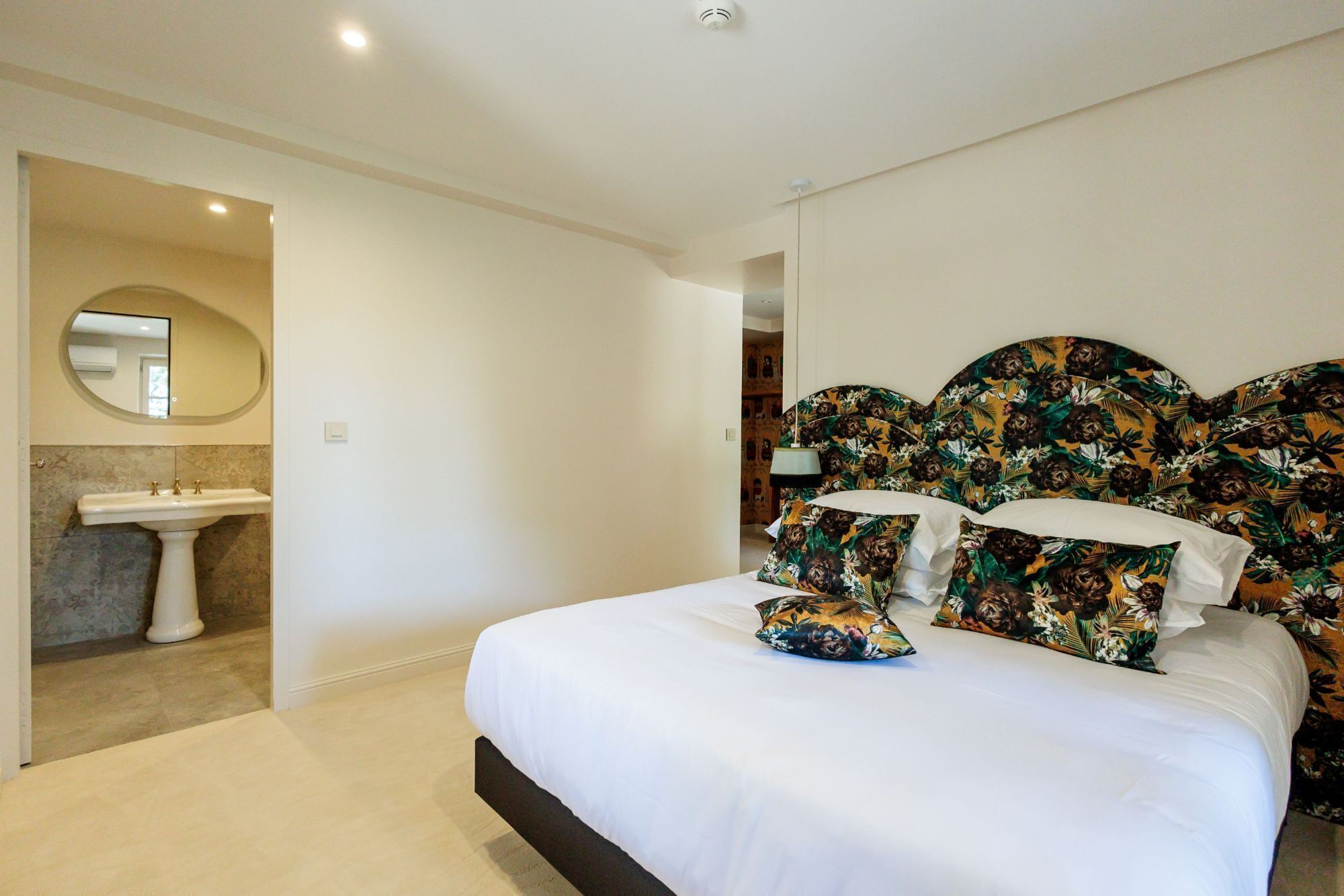 Un dormitorio con cama, espejo redondo, lavamanos y cabecera con estampado floral.