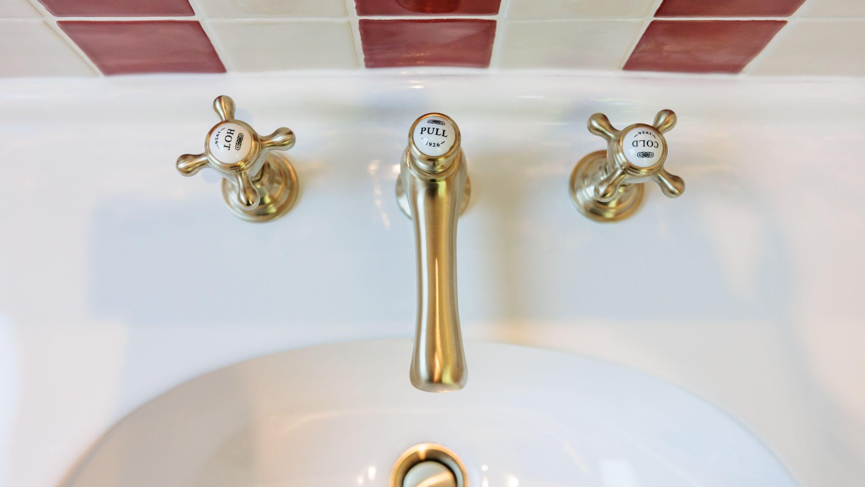 A bathroom sink with three gold-colored pull handles, each labeled with a function (HOT, PULL, COLD).