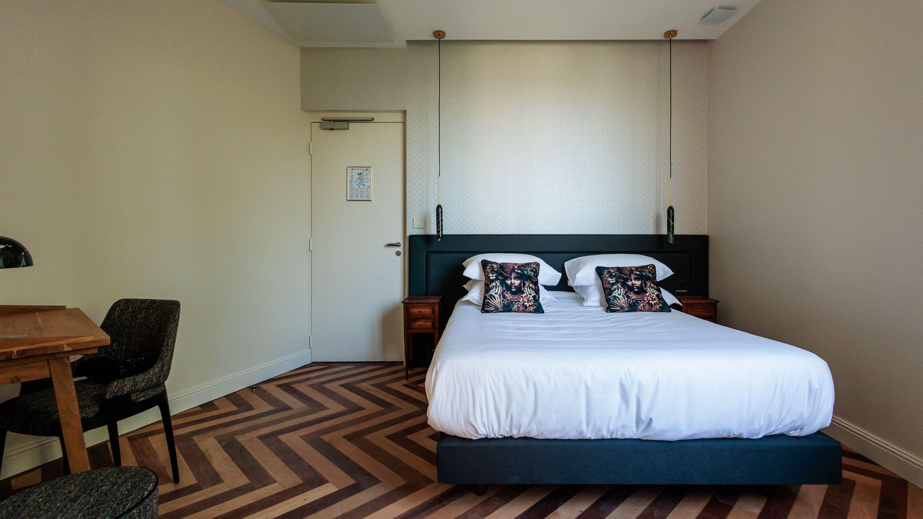 A hotel room with a bed, a desk, a chair, and a door.