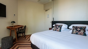 A hotel room with a bed, two pillows, a nightstand, a desk, a chair, and a trash bin. - La Villa Kara (Romans-sur-Isère)