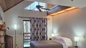Ein Schlafzimmer mit einem Bett, Nachttischlampen, einem Deckenventilator, einem Fernseher und einem Steinkamin.