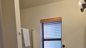 Ein Badezimmer mit Dusche, Waschbecken, einem Fenster mit Jalousien und einem Handtuchhalter.