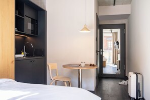 A hotel room with a bed, a small table with a chair, a microwave, a sink, and a suitcase. - STAYERY Fürth Innenstadt (Fuerth)