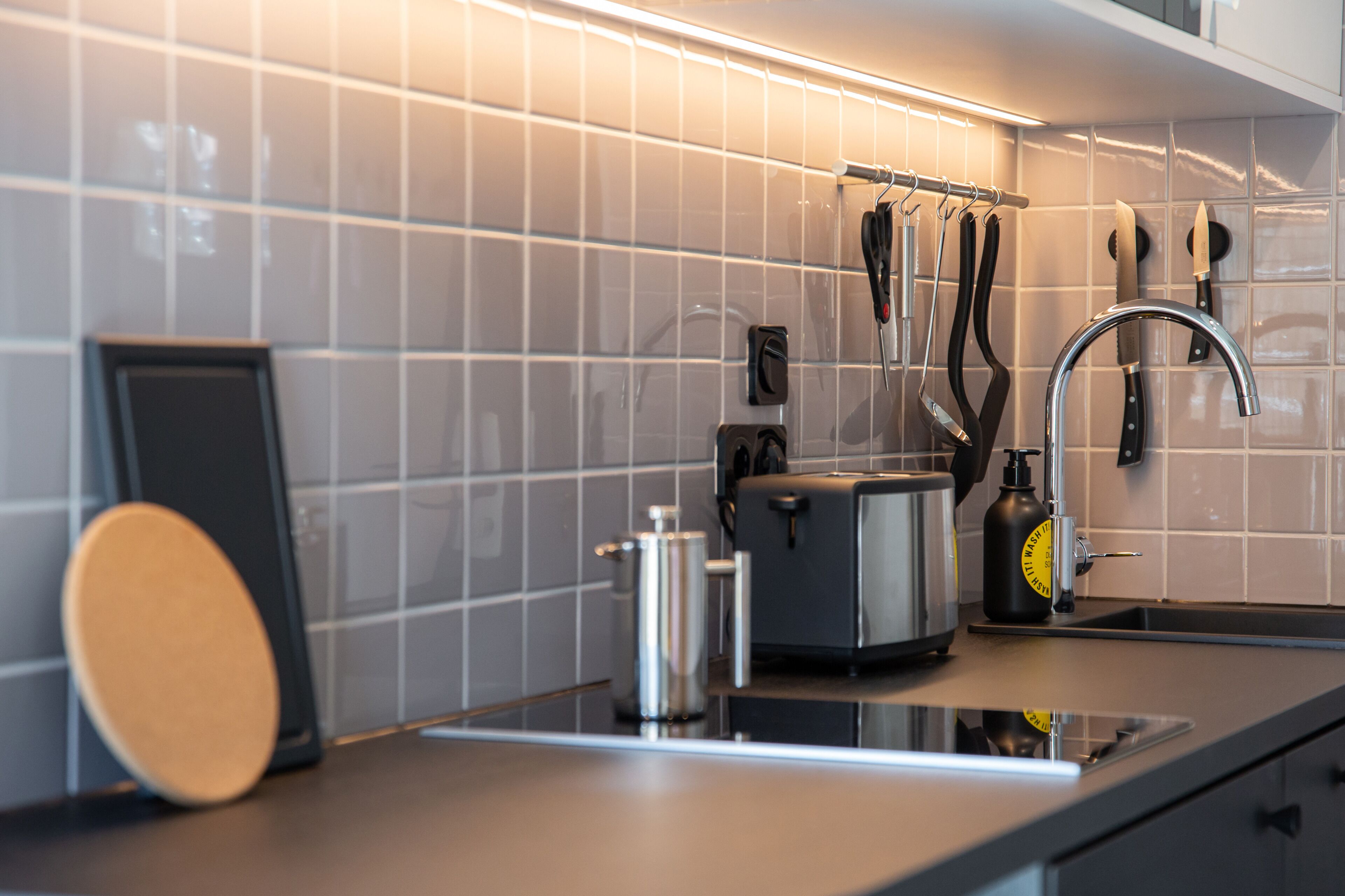 A modern kitchen with a tiled backsplash, a stainless steel toaster, a kettle, and a knife rack.