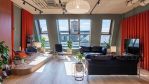 A modern living room with a black leather sofa, a coffee table, and a TV. There are two windows with red curtains, a plant, and a bookshelf. - STAYERY Fürth Innenstadt (Fuerth)