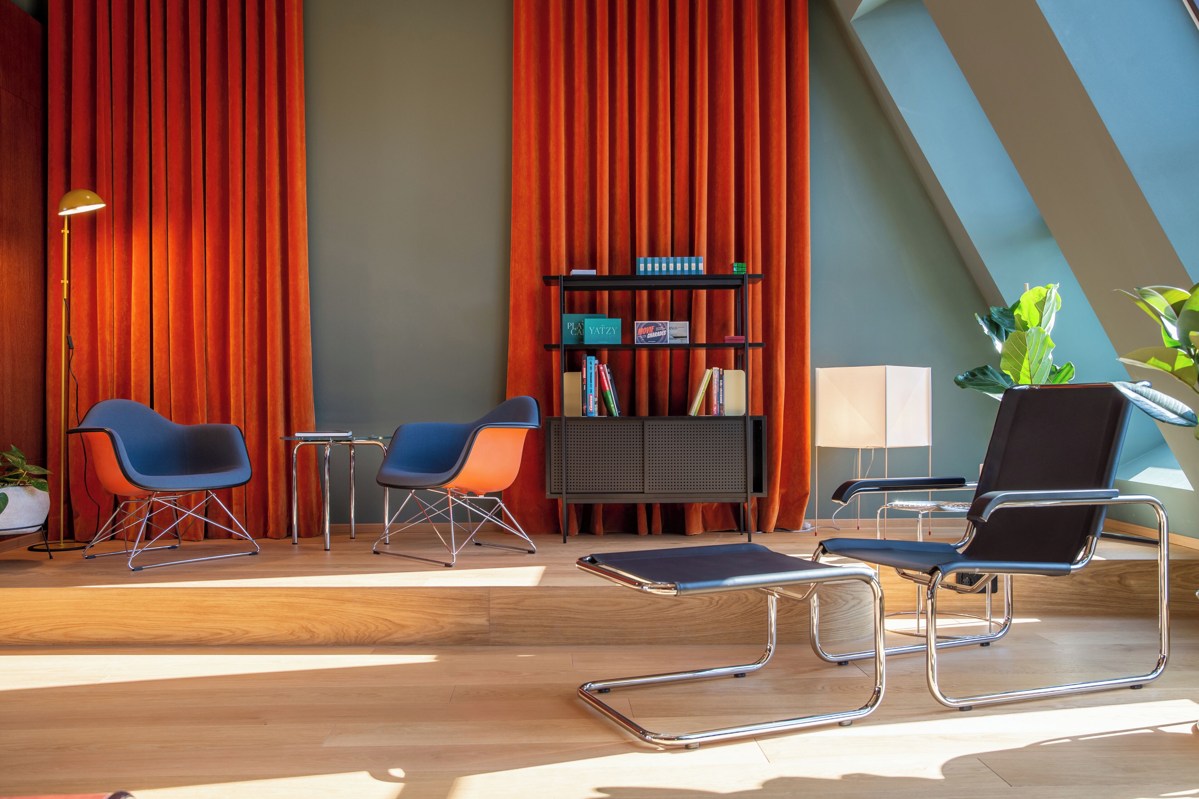 Una habitación moderna con piso de madera, dos sillas azules, una silla negra, una mesita, una estantería y una planta en maceta.