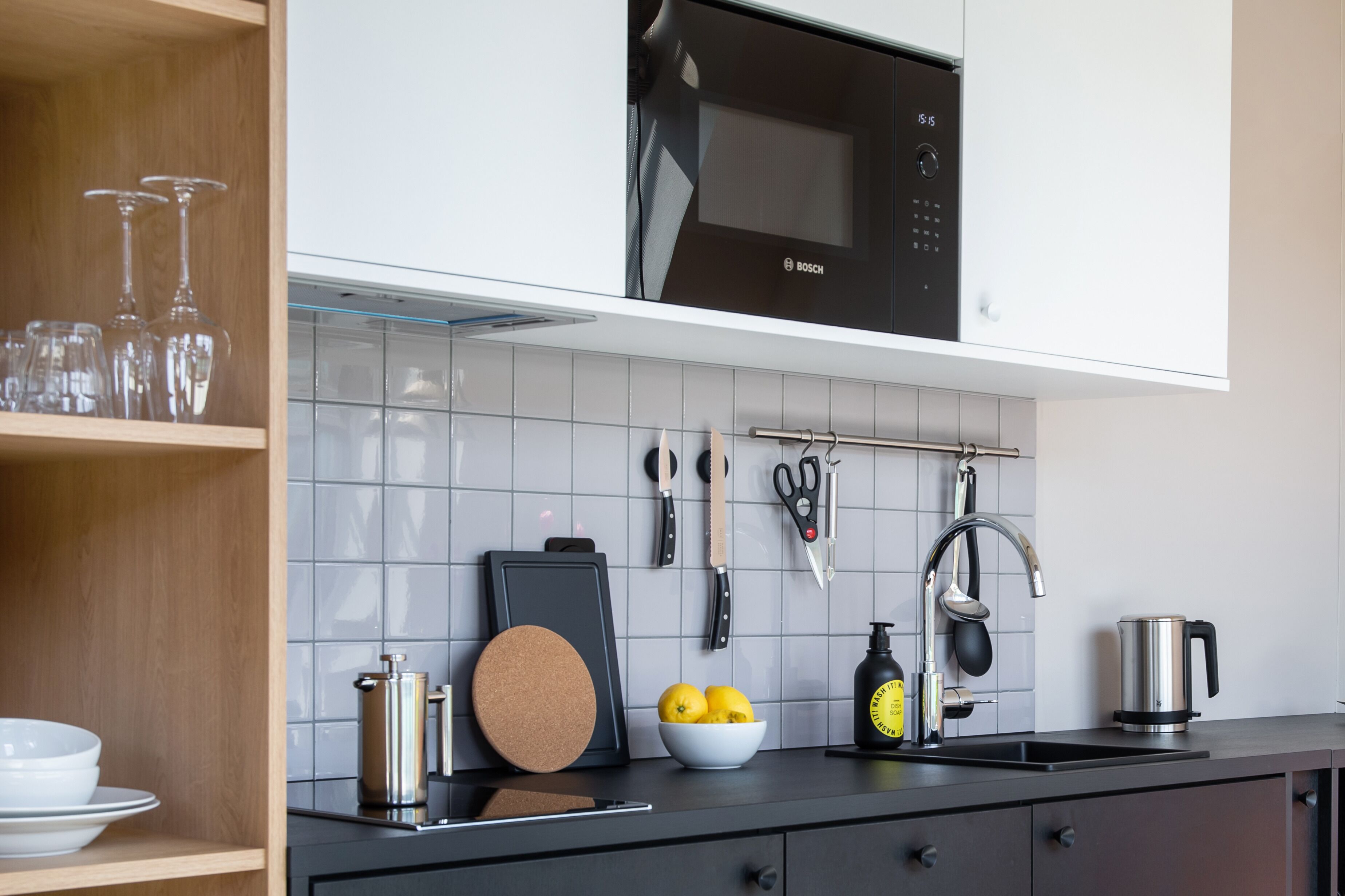 Een moderne keuken met een Bosch magnetron, een koffiezetapparaat en diverse keukengerei aan de wand.
