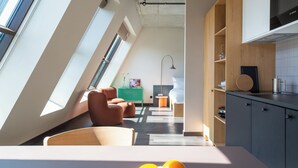 A modern kitchen with skylights, a dining area with a table and chairs, and a bedroom with a bed and bedside table. - STAYERY Fürth Innenstadt (Fuerth)