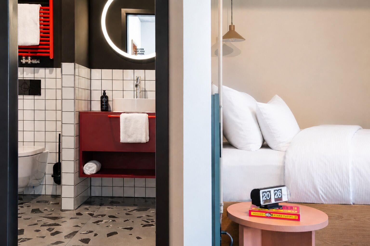 A hotel room with a bathroom, a bed, a bedside table, and a wall clock.