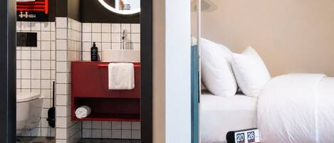 A hotel room with a bathroom, a bed, a bedside table, and a wall clock.