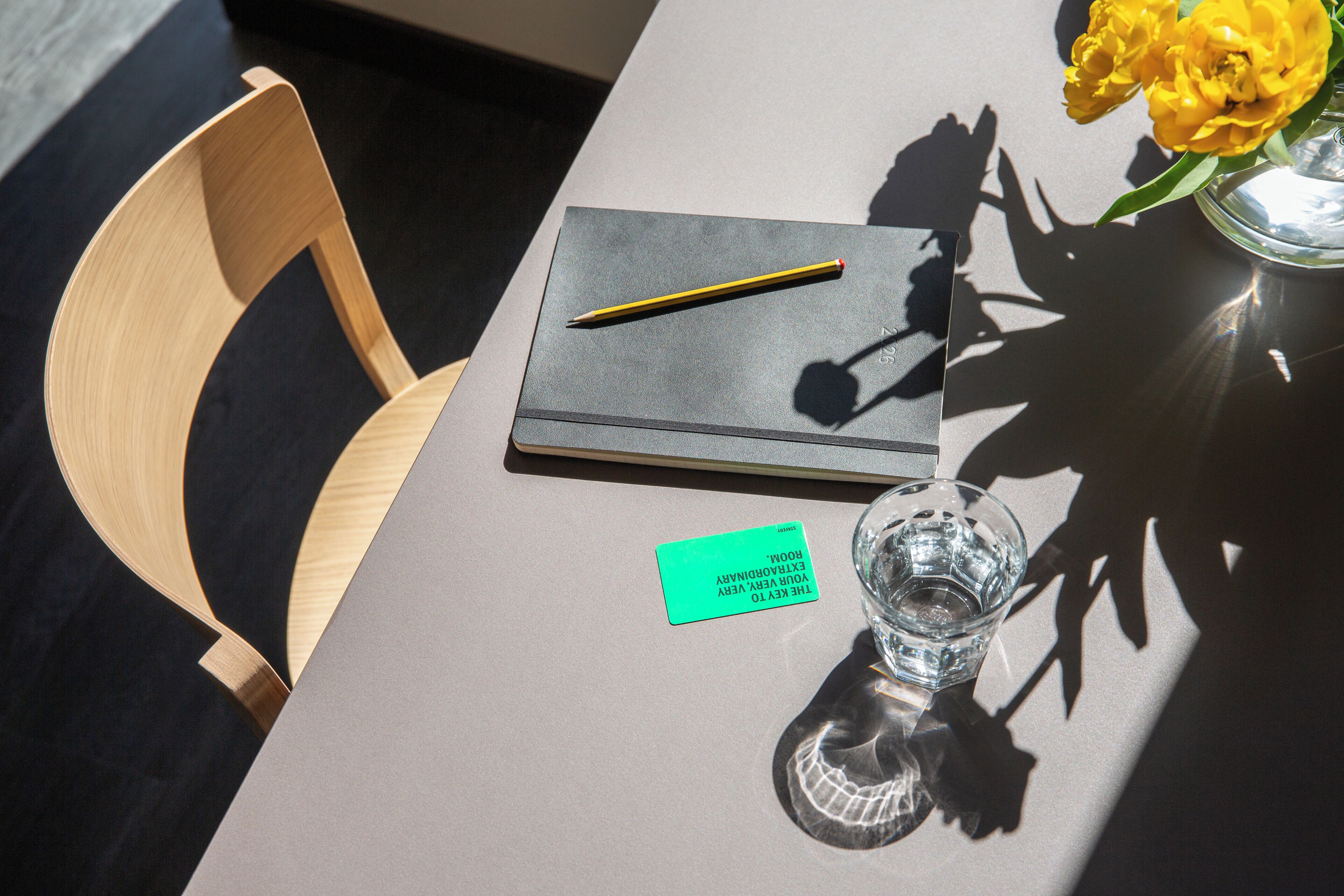 Una mesa con un cuaderno, un lápiz, un vaso de agua, una flor y una nota.