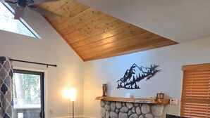 A living room with a stone fireplace, a ceiling fan, a TV on a wooden cabinet, and a patterned rug. - Comfortable 1-bedroom Suite (Idyllwild-Pine Cove)
