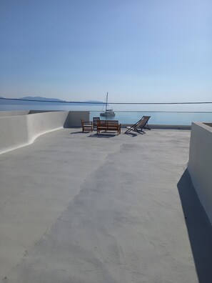 A rooftop terrace with a concrete floor, two wooden benches, a pair of lounge chairs, and a sailboat in the background. - Holiday Home 'I Have A Big Dream' with Sea View, Private Terrace and Air Conditioning (Agia Pelagia)