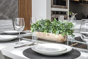 Una mesa de comedor dispuesta con platos, cubiertos y una maceta de madera con follaje verde.