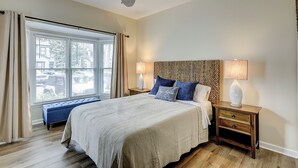 Un dormitorio con cama, mesitas de noche, lámpara, ventilador de techo y ventana con cortinas.