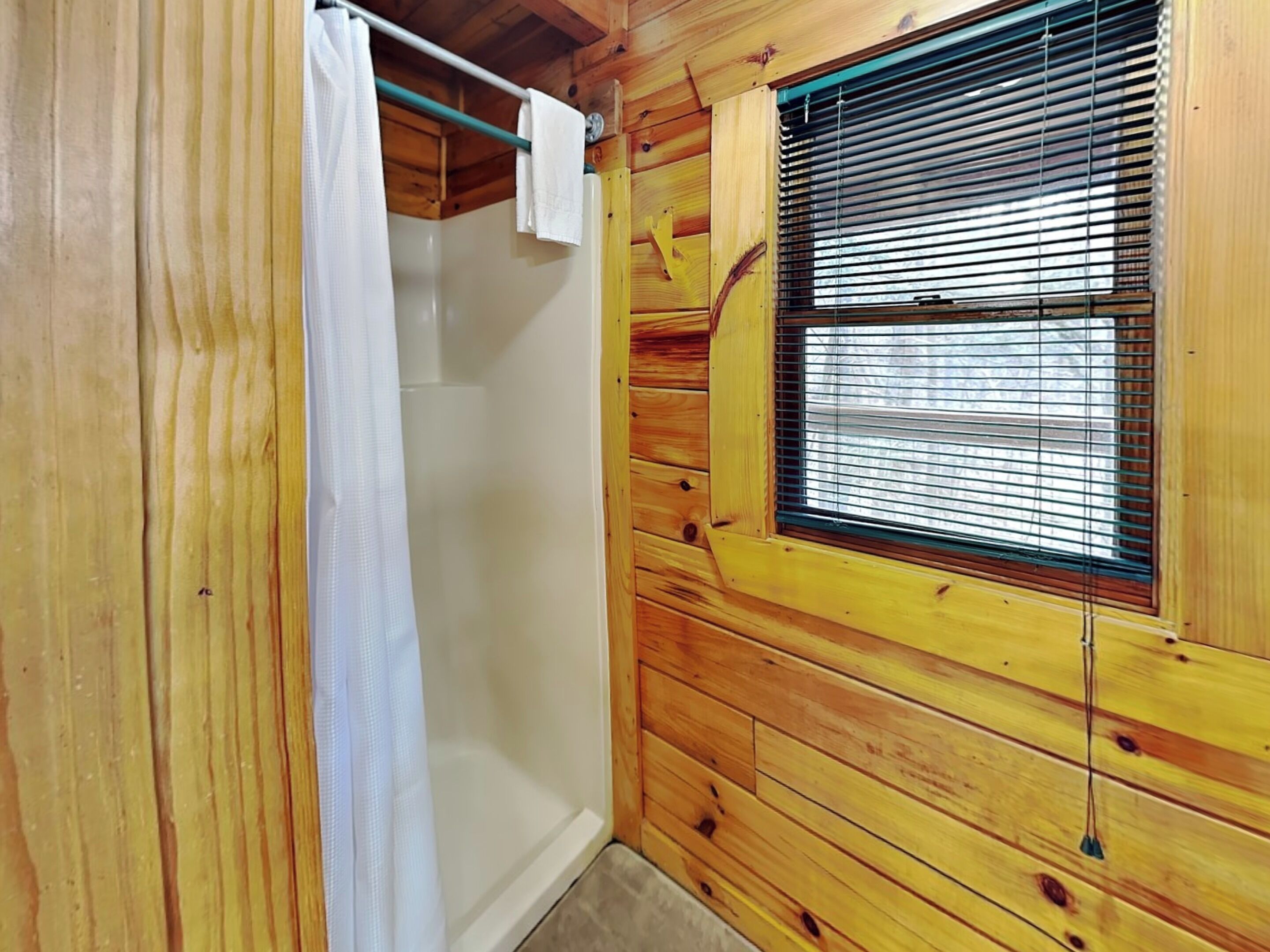 A wooden room with a window, a shower curtain, and a towel rack.