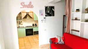 Un soggiorno con un divano rosso, una cucina visibile attraverso un arco e un cartello appeso al muro.