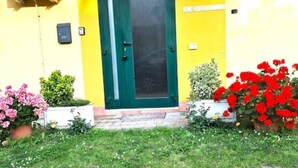 Un edificio giallo con una porta verde, piante in vaso e un piccolo giardino.