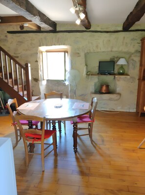 A dining area with a wooden table and chairs, a window, a fan, a television on a shelf, and a lamp. - Quercy House: Private Terrace, Garden & Balcony in the Célé Valley (Corn)