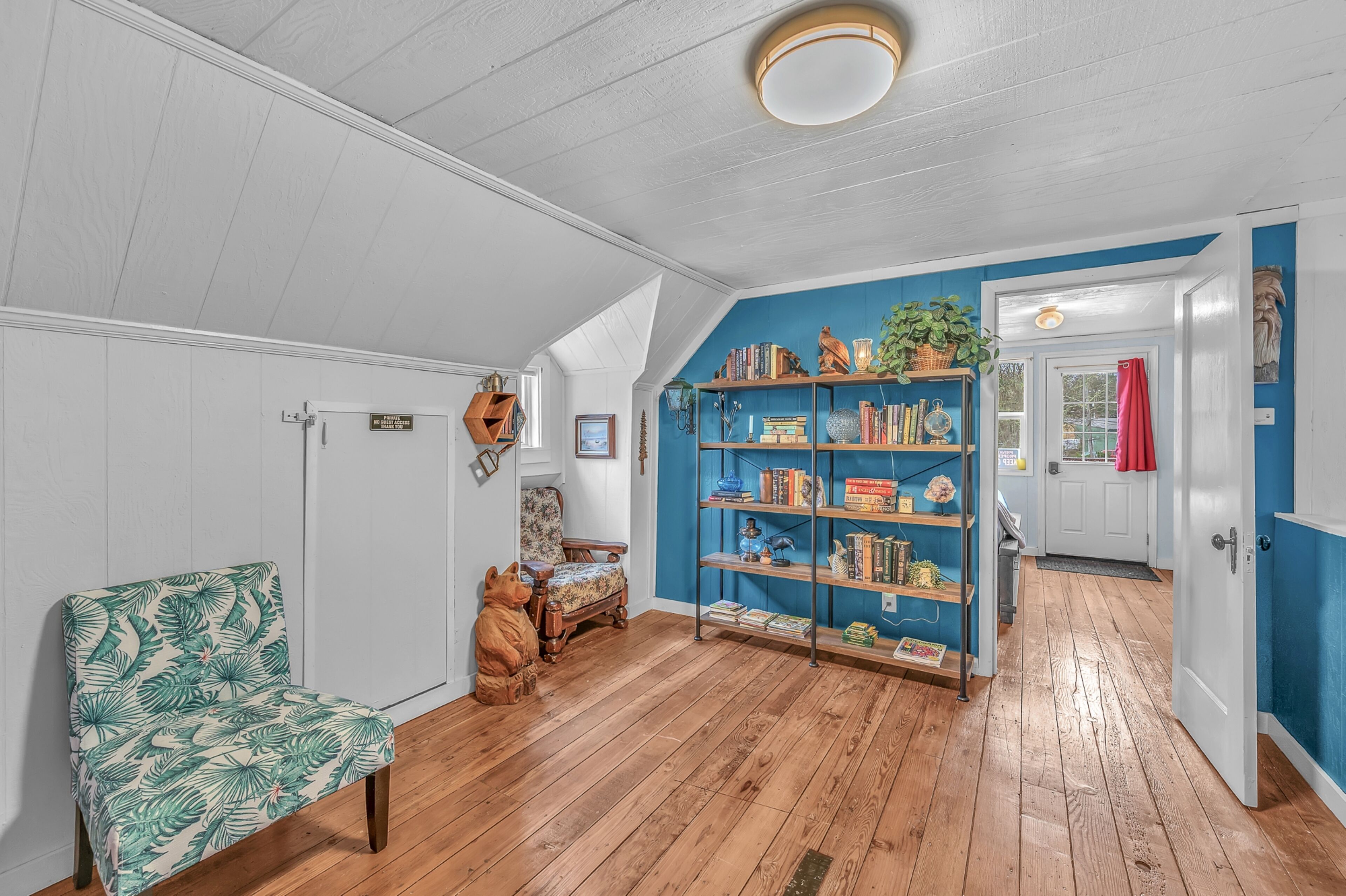A room with a wooden floor, a bookshelf, a chair, and a door.