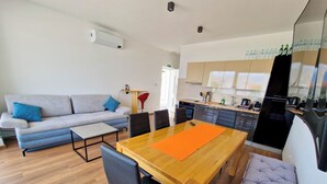 Et moderne opholdsrum med sofa, spisebord, stole og et tekøkken.