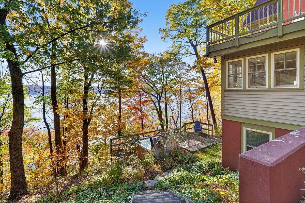 A house with a wooden staircase leading to a deck, surrounded by trees with autumn foliage.