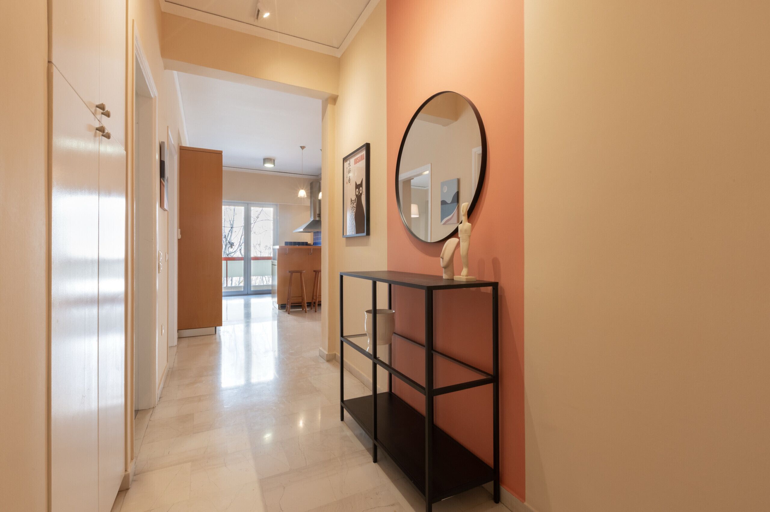 Un couloir avec une console noire, un miroir rond et un tableau encadré accroché au mur.