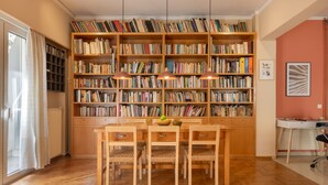 Ein Zimmer mit einem großen Bücherregal, einem Esstisch mit Stühlen und einer Heizung.
