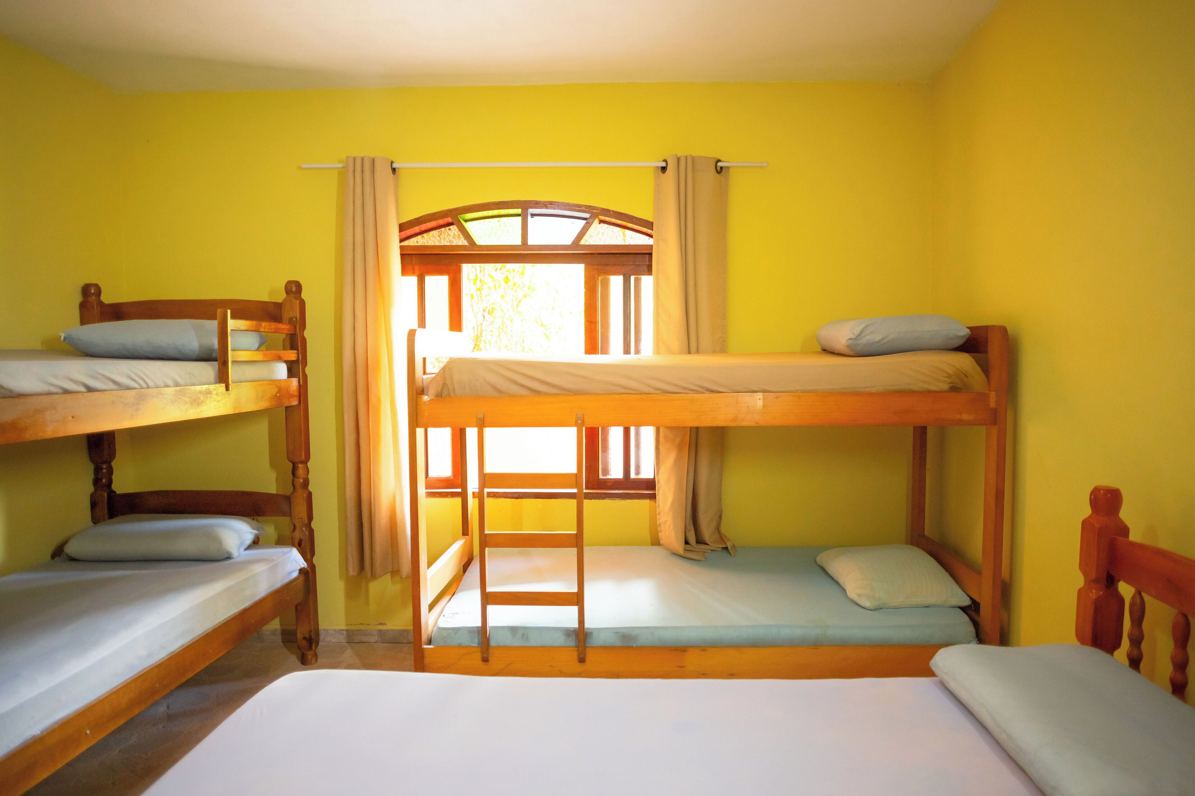 Dormitorio con literas, una escalera, cabecero de madera y ventana con cortinas.