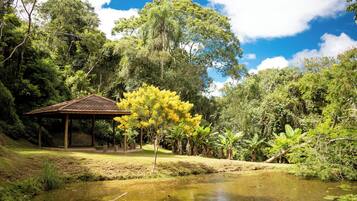 A pavilion with a tiled roof, surrounded by lush greenery and a pond.