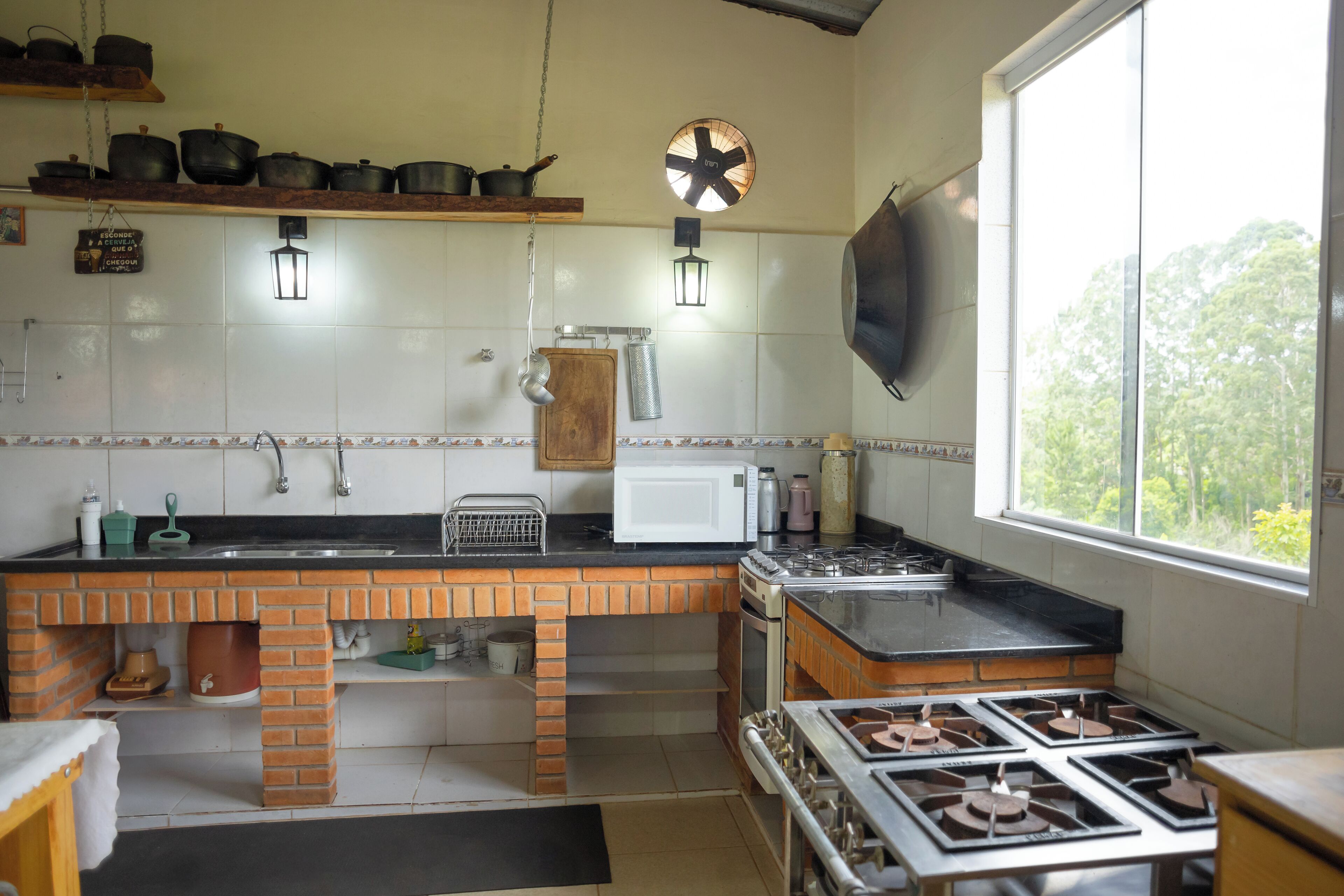 Cocina con mostrador de ladrillo, estufa, microondas y luces colgantes.