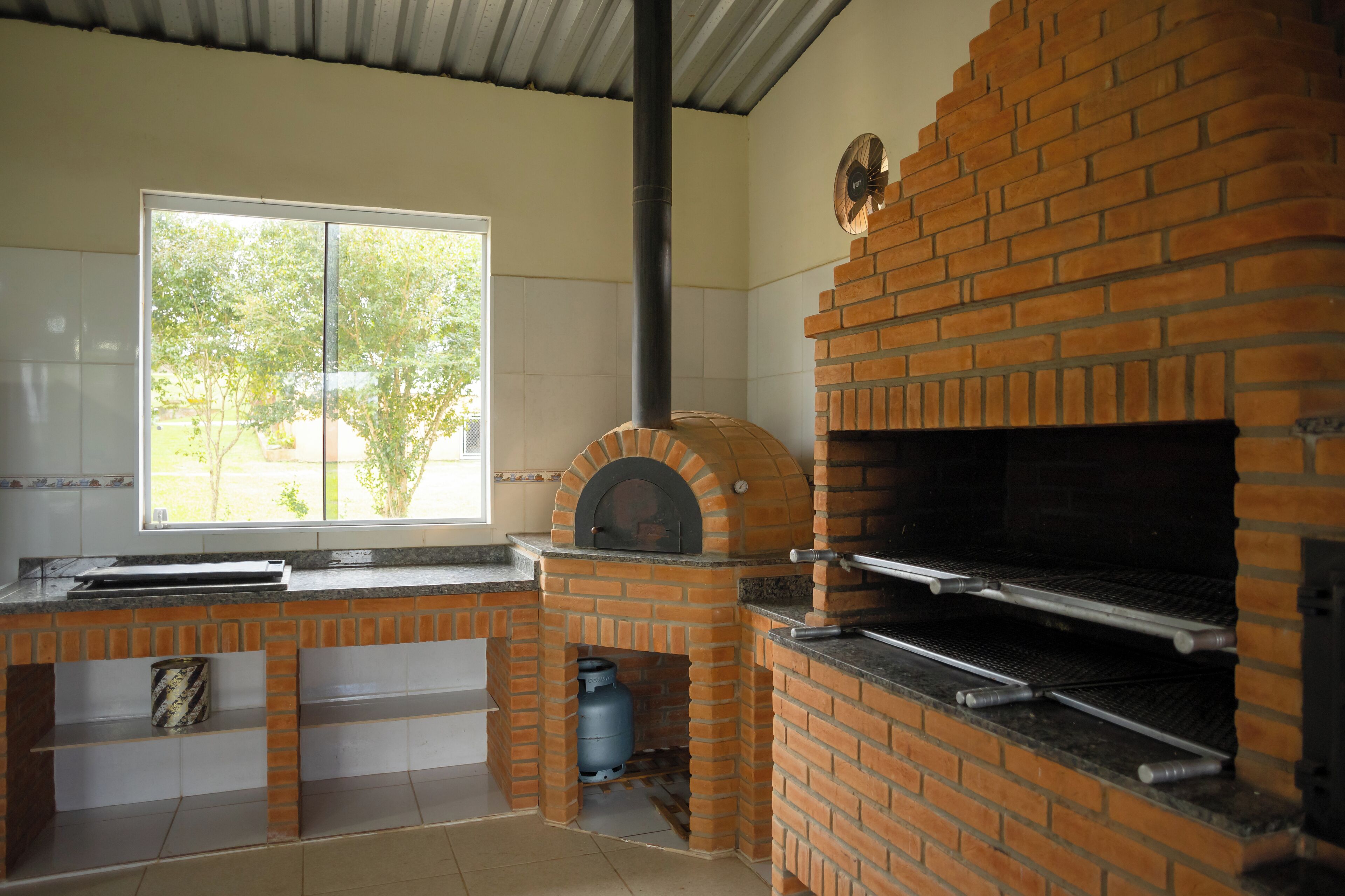 A kitchen with a brick oven, a window, and a view of trees.