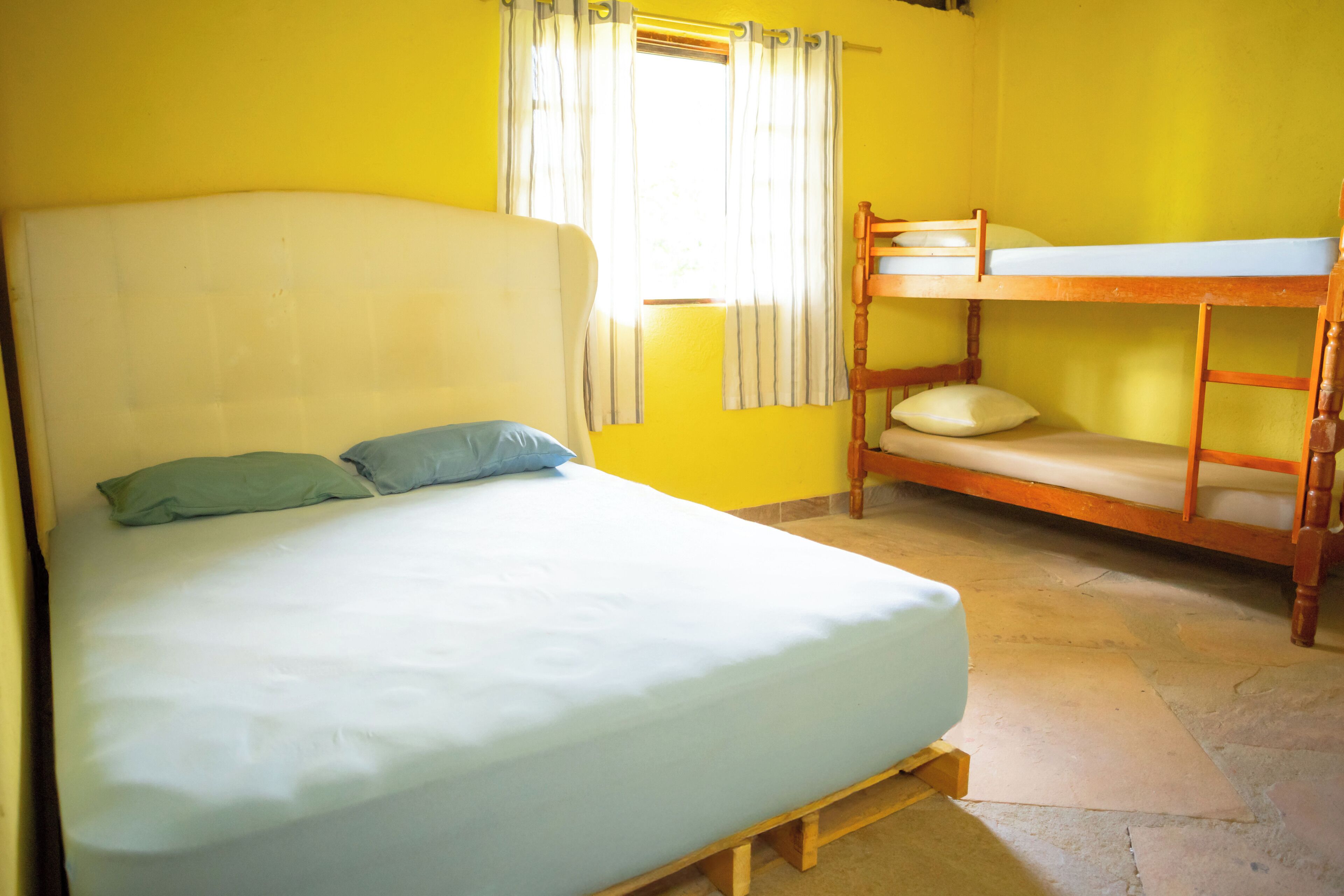 A room with a single bed, a bunk bed, a window with curtains, and a tiled floor.
