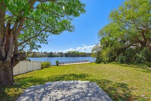 Un espacio verde con sendero pavimentado, un árbol y vista al lago.