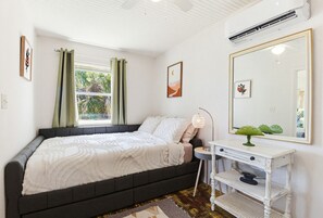 Ein Schlafzimmer mit einem Bett, einem Nachttisch, einem Spiegel und einem Fenster mit Vorhängen.
