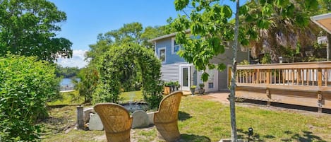 Ein Haus mit Terrasse, ein kleiner Garten mit Korbstühlen und ein Baum.