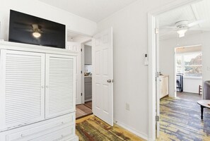 Ein Zimmer mit einem weißen Schrank, einem Fernseher und einer Tür, die in eine Küche führt.
