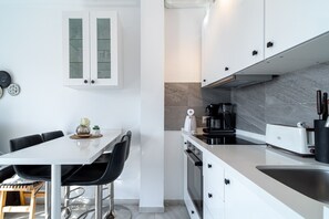 A modern kitchen with white cabinetry, a dining table with chairs, and a coffee machine. - Summer Azul 96 Casa Monica by Casasol (Nerja)