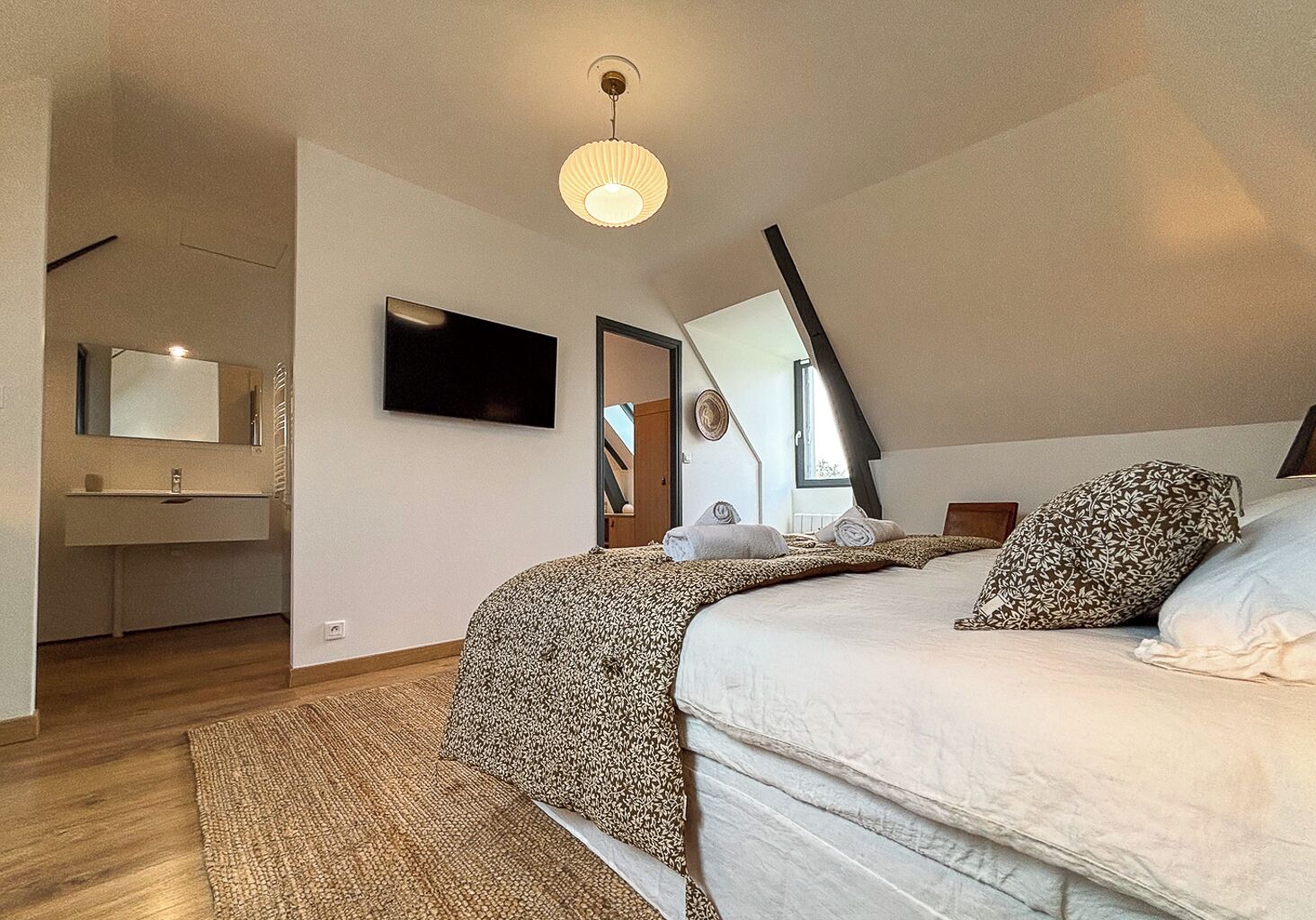 A bedroom with a bed, a TV, a mirror, and a window.