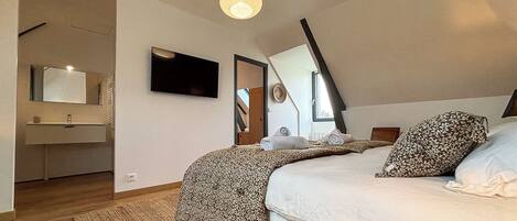 A bedroom with a bed, a TV, a mirror, and a window.