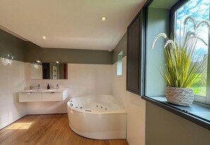 Une salle de bain moderne avec une baignoire sur pieds, un meuble-lavabo avec un miroir et une fenêtre donnant sur un espace verdoyant.