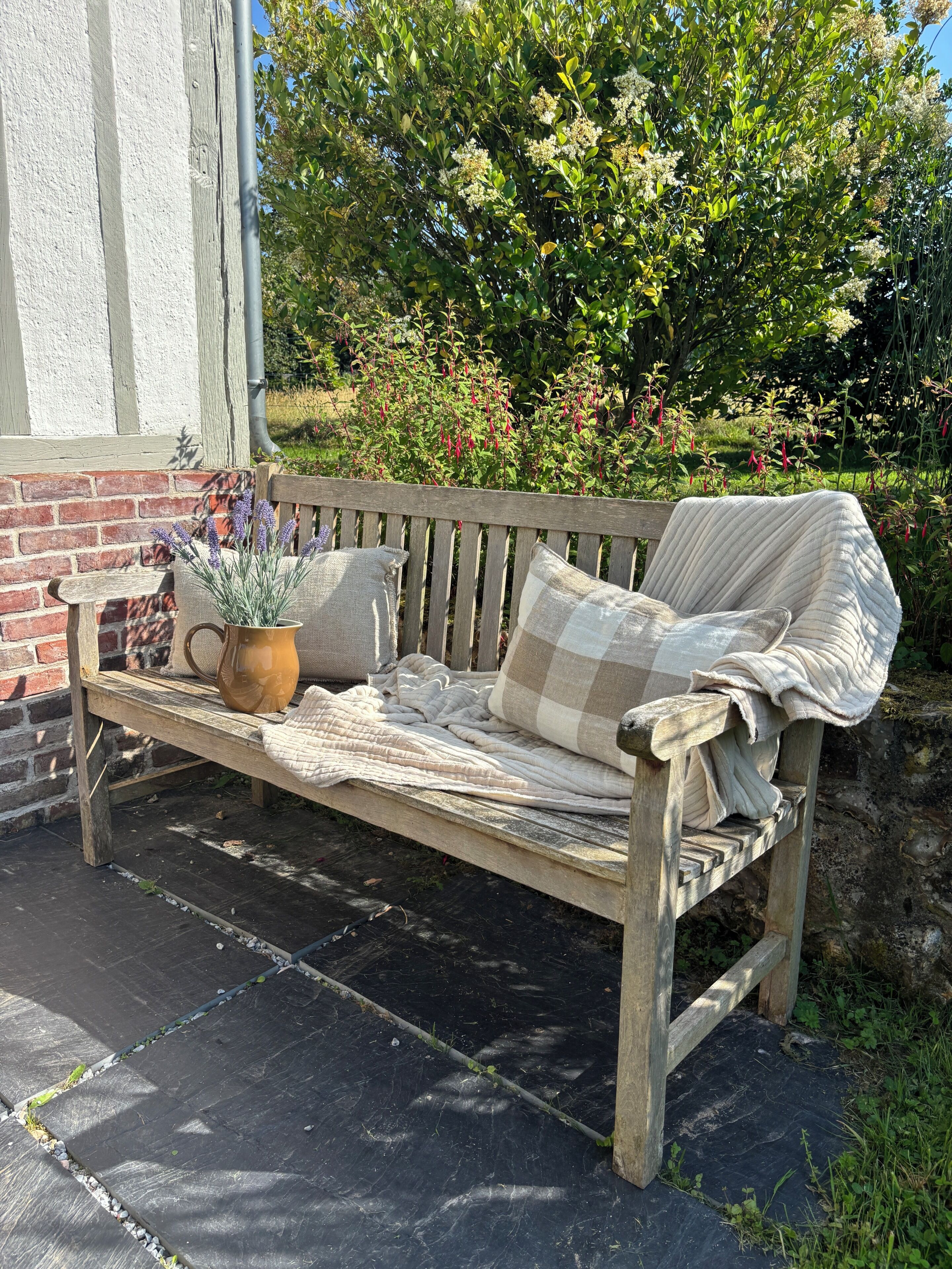 A wooden bench with a cushion and a potted plant.