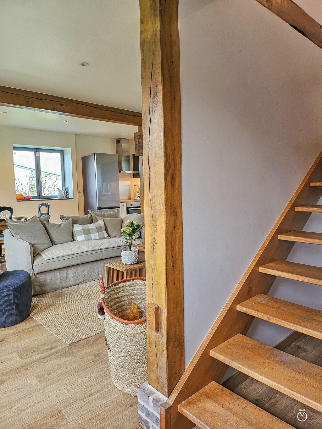 Un escalier avec des marches en bois menant à un palier, un canapé, une petite table avec un vase et une fenêtre donnant sur l’extérieur.